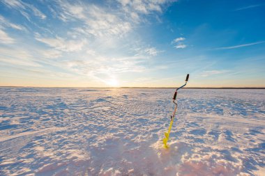 Donmuş bir gölün taze bir çukurunda, üzerinde sarı biti olan tek bir elle kumandalı buzluk duruyor. Uzun gölgeler öğleden sonra olduğunu gösteriyor. Rüzgâr tarafından oyulmuş kar ve kışın ortasında serin hava..