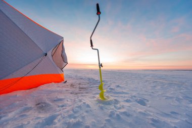 Parlak turuncu ve beyaz bir barınak donmuş bir gölün üzerinde duruyor. Sarı bir el çengelli matkabı güneşin doğuşunda taze bir deliğin yanında duruyor. Rüzgâr, kar ve pastel bir şafak ışığı oyuyor..