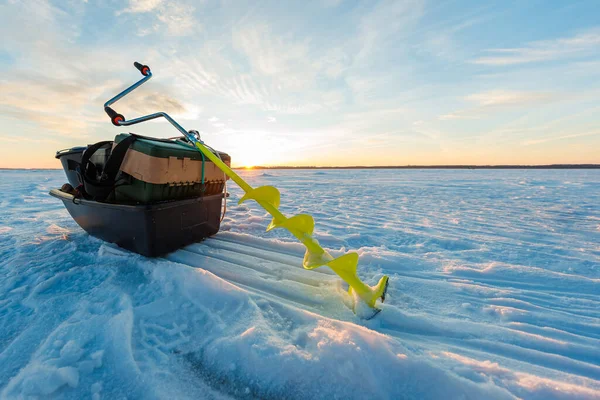 Sarı bıçaklı bir el kumandası, gün doğumunda donmuş bir gölün üzerindeki bir kızak ve alet çantasının yanında duruyor. Rüzgar şekilli kar dalgaları uzun gölgeli alçak güneşe çıkar..