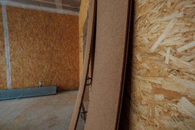 Çerçevelenmiş bir odada yakın görüntü OSB duvarlarını, kahverengi fiber panelleri, açıkta kalan kablo döngülerini ve duvar boşluklarının hazırlandığı metal yapı iskelesini gösterir..