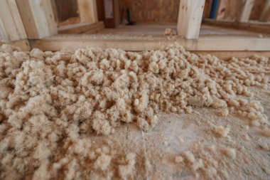 Zemin kat manzarası, çivili çiviler içindeki bir zemin üzerinde kabarık kahverengi ahşap fiber dolgu olduğunu gösteriyor. Kurucular, doğal ışık kullanımında termal ve akustik kullanım için yalıtım malzemelerini havaya uçurmaya veya elle paketlemeye hazırlar.