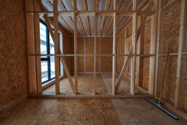 İnşaat halindeki ahşap çerçeve evin iç görünümü, marangozlar çerçeve oluşturma, OSB kaplama ve tavan kirişleri mevcut, iskele dışarıda, siyah pencere solda, cam sileceği sağda..