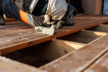 Eldivenli işçi, gün içinde kirişleri oymak için gizli klipsleri yerleştiriyor. Yakından bakınca tahıl, talaş, dizlik ve hassas alet teması görünüyor..