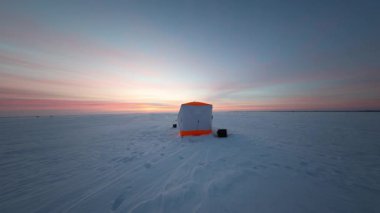 Güneş doğarken donmuş bir gölün üzerinde turuncu budanmış bir sığınak, iki siyah kızak, dağınık dişli, ayak izleri ve kızak izleriyle geniş açılı bir açıyla duruyor..