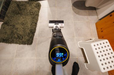 İlk bakışta açık gri fayansları hedef alan kablosuz bir yer temizleyicisi görülüyor. Beyaz bir taban kırmızı uyarı simgesi gösterir. Yeşil bir banyo paspası, beyaz bir tabure ve bir tuvalet görülebilir..