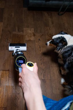 İçeride, bir insan paralı köpek saati olarak ahşap zeminde kablosuz ıslak kuru süpürge kullanır. Başa yakın ıslak yamalar, el simgesi yok, ve dairesel LED görüntü gücü ve modu gösterir.