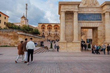 Corinthian sütunları ve kalabalık plaza manzaralı büyük taş geçit. Ziyaretçiler, öğleden sonra ışığı uzun gölgeler oluştururken katmanlı merdivenlere ve kavisli cephelere doğru yürürler..