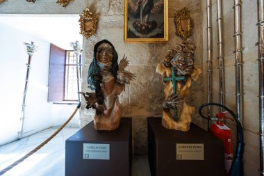 Santa Teresa de Jesus ve San Juan de la Cruz 'un iki ahşap büstü metal aksanlı, turkuaz haçlı, peçeli, gümüş şamdanlı ve kırmızı yangın söndürücülü kaidede dururlar..