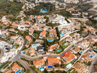 Terasotta çatıları olan İspanya yamaç manzaralı villalar, kavisli sürücüler, teraslı yamaçlardaki yumuşak gündüz ışığında birçok turkuaz havuz, palmiye ağaçları ve tenis kortu..