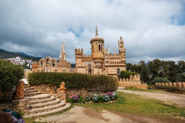 Benalmadena 'daki Castillo Monumento Colomare taretleri, tepeleri ve kemerleri olan bir tepede duruyor. Ziyaretçiler, Sierra de Mijas 'ı çevreleyen bulutlar gibi yatakların ve merdivenlerin arasında yürüyor.