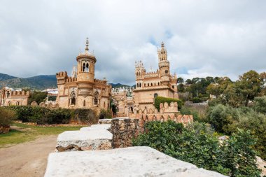 Benalmadena, İspanya 'daki Castillo Monumento Colomares Neo Mudejar kulelerini, çentikli duvarları, süslemeli kuleleri ve bulutlu ışık altında taş bir yoldan görünen oymaları gösteriyor..