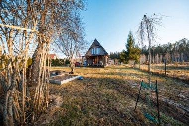 Yapraksız ağaçlar, kazıklı bir kozalaklı kozalaklı ağaç ağaçları, yükseltilmiş bahçe yatakları, oyuncaklar ve uzun gün gölgeleriyle kaplı, geniş bir buz örtüsü altında bir çerçeve..