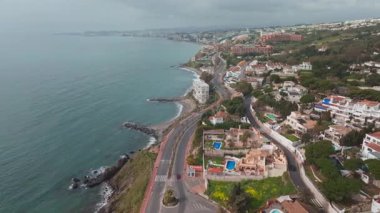 İspanya 'daki hava aracı görüntüsü palmiye güvertesi, terracotta villaları, uçurum kenarı blokları, kayalık kayalıklar, sessiz turkuaz deniz, hafif dalgalar ve hafif bulutlu ışık trafiği gösteriyor..