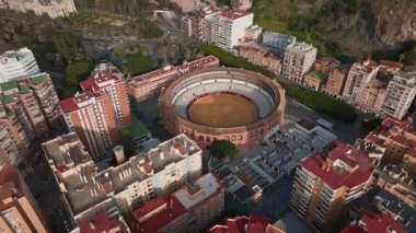 Malaga 'daki Plaza de Toros de La Malagueta' nın havadan görünüşü boş katlar, kumlu arena, yakınlardaki liman, palmiye kordonları, yatlar ve sıcak altın saat ışığı.
