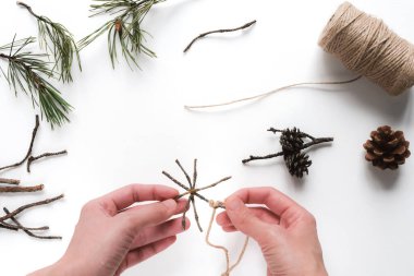 Eller, dalların doğal çevre dostu malzemelerinden ev yapımı Noel ağacı oyuncağı yapıyor. Üst görünüm, düz görünüm, seçici odak.