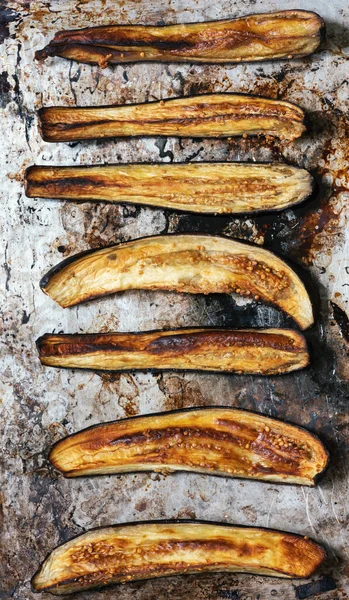 Baked eggplant wedges on an old soiled baking sheet. Top view, flat lay, vertical format.