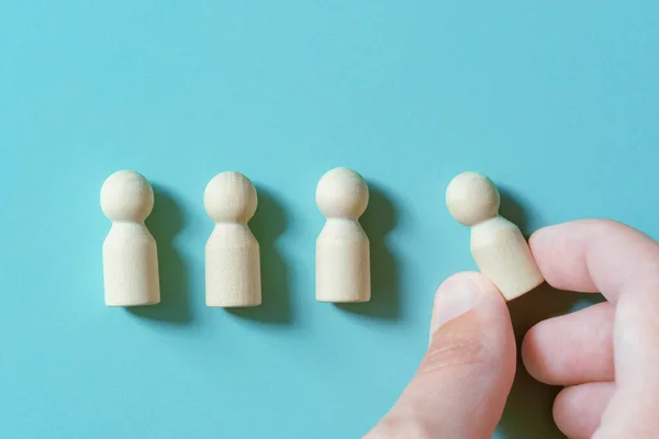 A row of wooden figures and a hand moving them. Society, demography or hiring for work concept figures of people symbol on the green-blue background with copy space