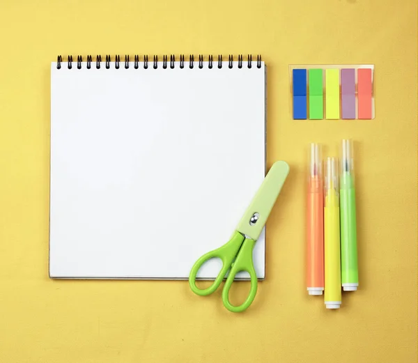 Sarı arka planda beyaz not defteri ve işaretler. Kırtasiyeli sarı arkaplan ve ilkbaharda bir defter, okul işleri ve öğrenim kavramı.