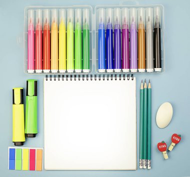 Ortasında not defteri, renkli kalemler ve kalemlerle mavi parlak bir arka planda kırtasiye malzemeleri. Okula dönelim. Okul öğrenme konsepti. Boşluğu kopyala.