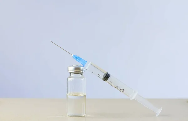 Açık bir sıvıyla cam ampul masanın üzerinde şırıngayla birlikte. Ampulün yanındaki şırınga.