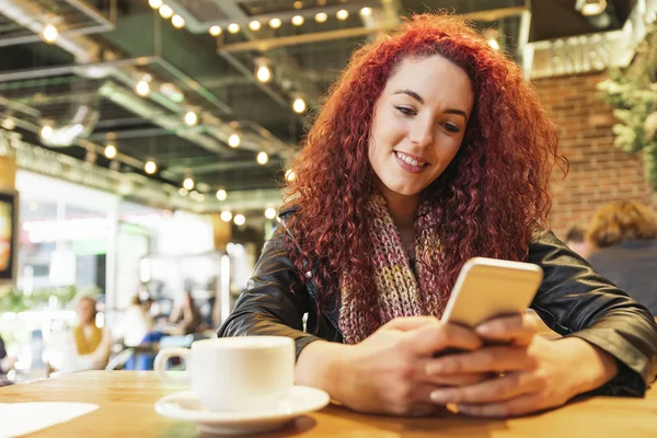 Jeune femme assise dans un café branché écrivant avec son téléphone portable — Photo