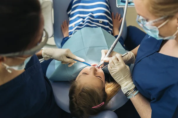 Dentists with a patient during a dental intervention to girl. — Stock Photo, Image