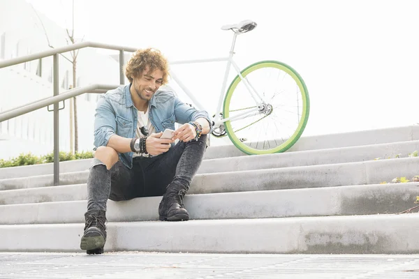Όμορφος νεαρός άνδρας με κινητό τηλέφωνο και στάσιμου ποδηλάτων. — Φωτογραφία Αρχείου