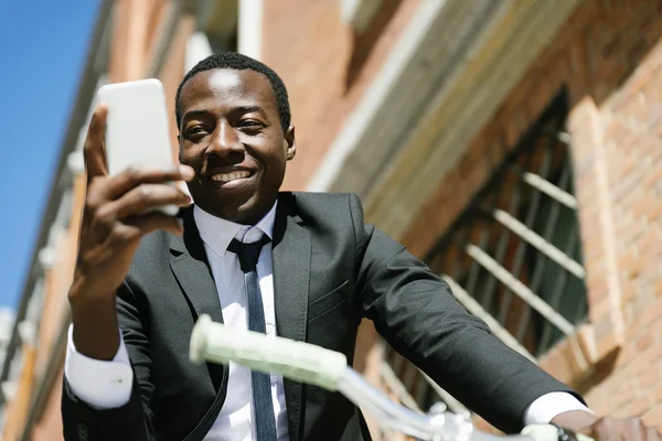Bonito homem africano sorrindo quando ele está usando seu celular . — Fotografia de Stock