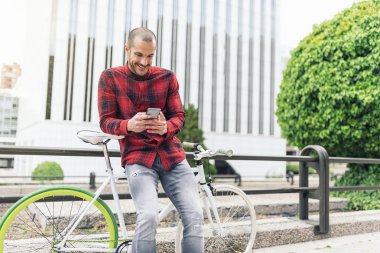 Genç adam cep telefonu ve sabit vites bisiklet.