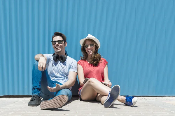 Счастливая привлекательная молодая пара сидит и смеется над голубым — стоковое фото