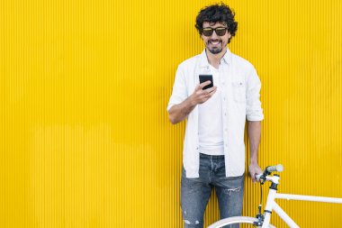 Yakışıklı genç adam cep telefonu ve sabit vites bisiklet.