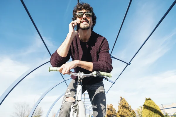 Красивый молодой человек с мобильным телефоном и велосипедом с фиксированной передачей . — стоковое фото