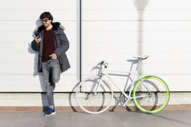 Yakışıklı genç adam cep telefonu ve sabit vites bisiklet.