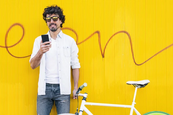 Όμορφος νεαρός άνδρας με κινητό τηλέφωνο και στάσιμου ποδηλάτων σε t — Φωτογραφία Αρχείου