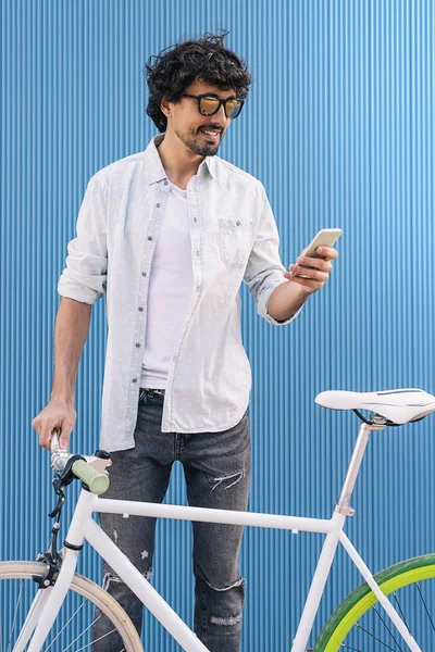 Красивый молодой человек с мобильным телефоном и велосипедом с фиксированной передачей . — стоковое фото