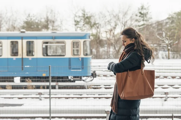 Wanita muda dalam mantel musim dingin mencari arlojinya menunggu kereta . — Stok Foto