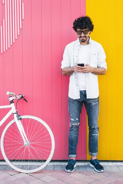 Όμορφος νεαρός άνδρας με κινητό τηλέφωνο και στάσιμου ποδηλάτων. — Φωτογραφία Αρχείου