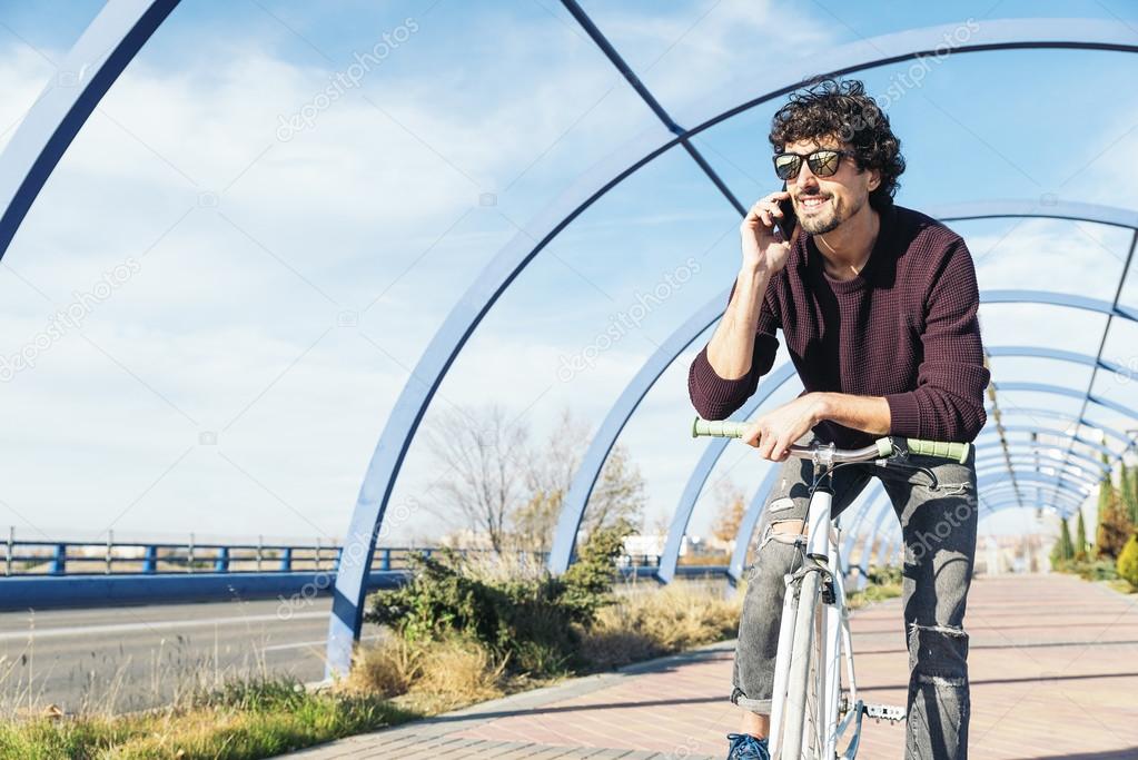 Handsome young man with mobile phone and fixed gear bicycle in t