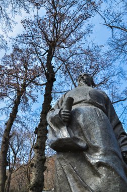 Çıplak ağaçlara ve mavi gökyüzüne karşı taş Çin heykeli. Suzhou, Çin.