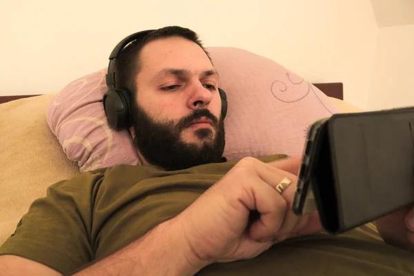 young man with beard is lying on his belly in bed and using laptop, selective focus.green screen