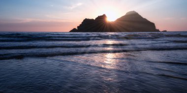 Güneş batarken Holywell körfezi, Cornwall, İngiltere, Carter Adaları 'nın üstünde.