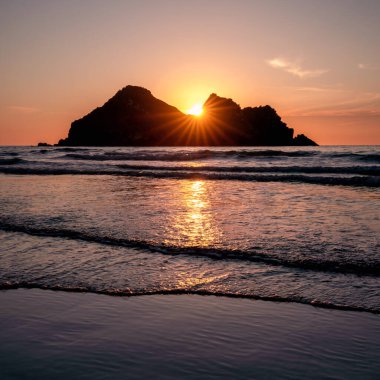 Güneş batarken Holywell körfezi, Cornwall, İngiltere, Carter Adaları 'nın üstünde.
