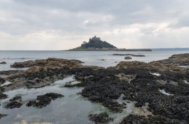 Cornwall İngiltere 'deki muhteşem St. Michaels binası. Marizion limanından bakan kayalardan oluşan bir ön planda.
