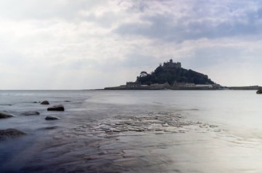 Cornwall İngiltere 'deki muhteşem St. Michaels binası. Marizion limanından bakan kayalardan oluşan bir ön planda.