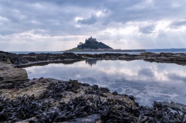 Cornwall İngiltere 'deki muhteşem St. Michaels binası. Marizion limanından bakan kayalardan oluşan bir ön planda.