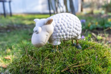 Stockholm, İsveç - 1 Nisan 2021: Bahçedeki ilk bahar çimlerinde bulanık arka planda duran küçük koyun figürü
