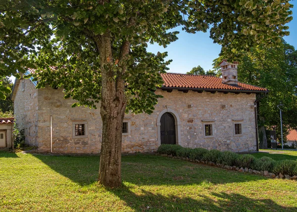 Lipica, Slovenya - 8 Ağustos 2025 Taş şapeli Ağaçlar ve çimlerle çevrili kırmızı kiremitli çatı.