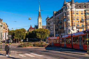 Stockholm, İsveç - 3 Ekim 2025: Kırmızı tramvayı, tarihi binaları ve kilise kulesi olan canlı bir şehir caddesi.