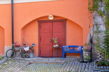 Vaxholm, İsveç - 13 Eylül 2025: Kırmızı kapılı, mavi banklı ve bisikletli büyüleyici avlu.