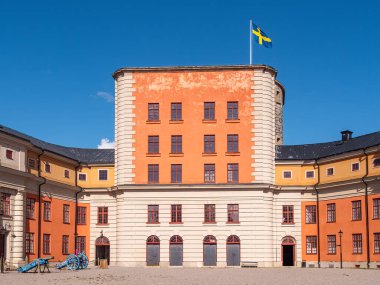 Vaxholm, İsveç - 13 Eylül 2025: Üzerinde İsveç bayrağı bulunan, merkezi kulesi ve simetrik kanatları olan, açık mavi gökyüzüne karşı kurulmuş tarihi bir bina.